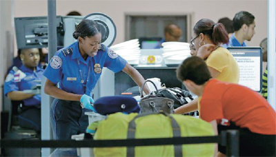 미 연방 교통안전국 직원이 공항 검색대에서 승객들의 가방을 검사하고 있다