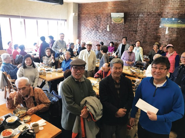 2019년 노인회 회원들에게 식사대접을 하고 함께 촬영한 타미 신(사진 오른쪽) 대표(보스톤코리아 자료사진)