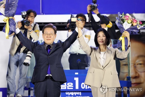 제21대 대통령 당선이 확실시되는 더불어민주당 이재명 대선 후보와 부인 김혜경 여사가 4일 서울 여의도 국회 인근에서 당 주최로 열린 국민개표방송 행사에 참석해 꽃다발을 받고서 시민들을 향해 두 팔을 들어올려 인사하고 있다.
